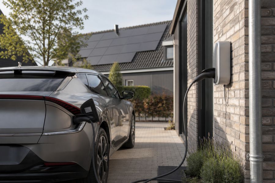 Auto aan een thuislaadpaal met zonnepanelen op het dak.